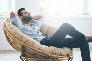 Total relaxation. Handsome young man keeping eyes closed and holding hands behind head while sitting in big comfortable chair at home